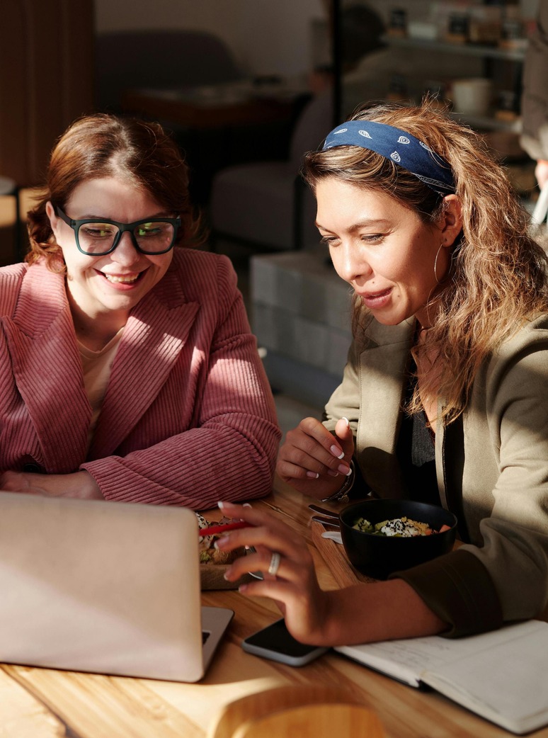 Two professionals sitting together at a table with a laptop, notebook, and food, collaborating and networking, representing online MBA student engagement.